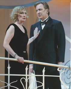 a man and woman in formal wear standing on a balcony looking off into the distance