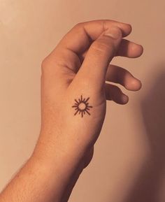 a person's hand with a small sun tattoo on their left wrist and the other arm