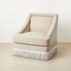 an upholstered chair with fringe trim around the legs and foot rests on a wooden floor