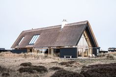 a black house with a thatched roof in the middle of an open field,