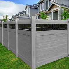 a gray fence in front of a row of houses with green grass on the ground