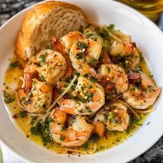 a white bowl filled with shrimp and pasta on top of a table next to bread