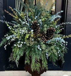 a potted plant with pine cones and greenery in front of a black door