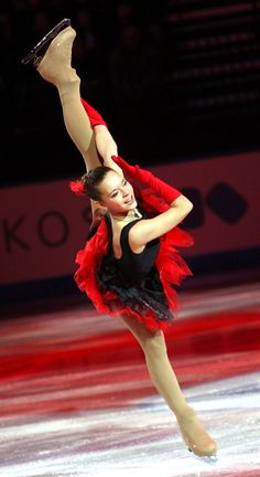 a female figure skating on the ice in a red and black outfit with her arms up