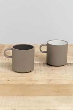 two coffee mugs sitting on top of a wooden table next to eachother