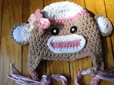 a crocheted monkey hat with pink and white stripes on the front, sitting on a wooden surface