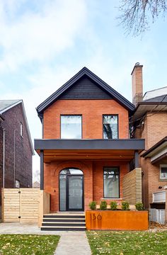 a brick house with a black roof and stairs leading up to the front door on a sunny day