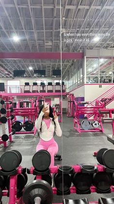 a woman taking a selfie in front of a mirror with pink equipment behind her