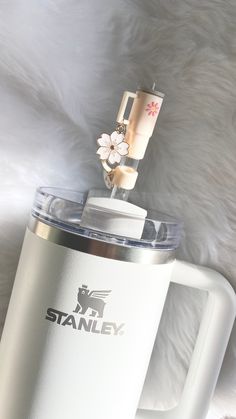 a white coffee mug with a flower on top and the word stanley written in black