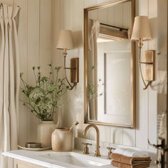 a bathroom sink sitting under a mirror next to a vase with flowers on top of it