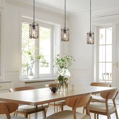 a dining room table and chairs in front of two windows with potted plants on them