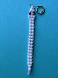 a white beaded keychain hanging from a hook on a blue surface with a pair of scissors