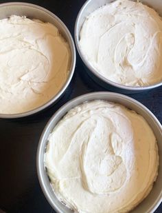 four pans filled with white frosting sitting on top of a table