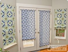 two windows with blue and white curtains in front of them, next to a wooden table