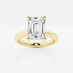 a yellow gold ring with an emerald cut diamond in the center, on a white background