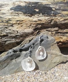 two silver earrings sitting on top of a rock