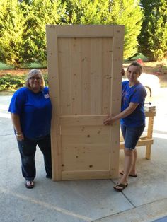 two women standing next to each other near a large wooden door on the side of a road