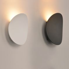 two wall lights mounted to the side of a white wall next to a round mirror