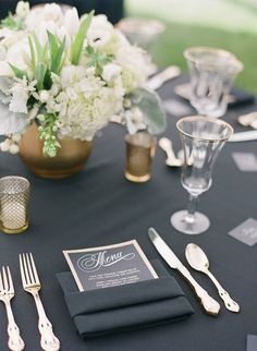 the table is set with silverware, napkins and flowers in gold vases