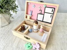 an open wooden box with toys in it on a table next to a potted plant