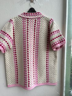 a pink and white crocheted sweater hanging on a wall