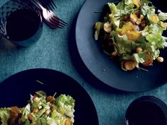 two black plates topped with salad next to wine glasses and utensils on a blue table cloth