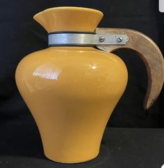 a yellow vase with a wooden handle and metal ring around it's neck, on a black background