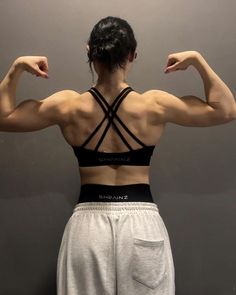 a woman showing off her back muscles in front of a gray wall and grey background