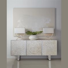 a white vase sitting on top of a dresser next to two lamps