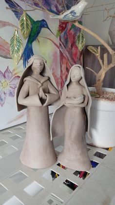 two ceramic figurines sitting next to each other in front of a painting on the wall