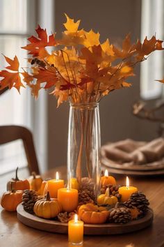 a wooden table topped with a vase filled with autumn leaves and candles next to pumpkins