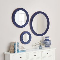 two blue and white circular mirrors on the wall next to a dresser with vases