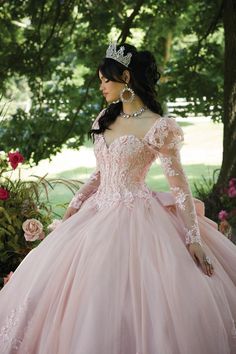 a woman in a pink ball gown with a tiara on standing next to some trees