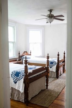 two beds in a room with wooden floors and ceiling fans on the windowsills