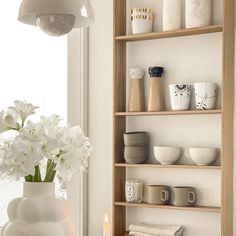 a vase with white flowers sitting on top of a table next to a shelf filled with dishes