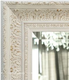 an ornate white framed mirror hanging on a wall