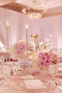 the table is set with white and pink flowers in vases, silverware, and candles