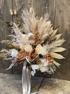 an arrangement of dried flowers and feathers in a vase on a counter top with a wooden background