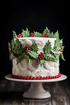 a christmas cake decorated with holly leaves and red berries sits on a white pedestal in front of a black background