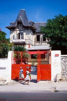 two people are walking into an open gated area in front of a large house