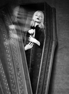 a black and white photo of a woman in a dress looking out from behind a mirror