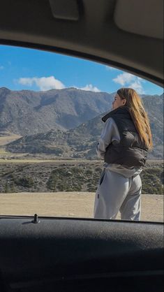 a woman standing in the back seat of a car looking out at mountains and hills