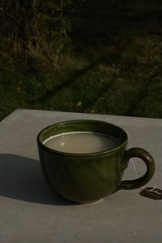 a green coffee cup sitting on top of a cement table next to a remote control