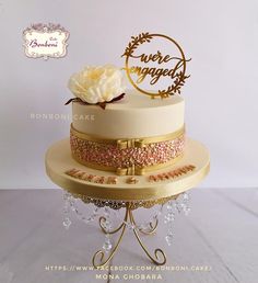 a three tiered cake decorated with gold and pink frosting, topped with a white flower