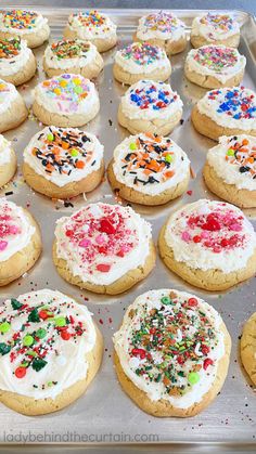 cookies with white frosting and sprinkles are on a baking sheet lined with confetti