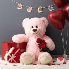 a pink teddy bear sitting on top of a bed next to red heart shaped balloons