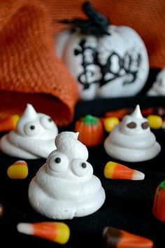 some white frosted pumpkins and candy on a black table with other halloween candies