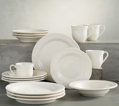 white dishes and cups are stacked on top of each other in front of a gray wall