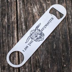 a bottle opener with the words i am the master on it sitting on top of a wooden table