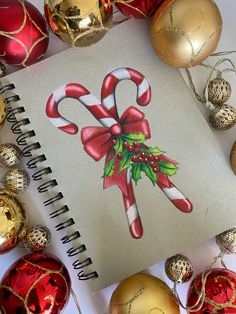 a drawing of a candy cane on top of christmas decorations and ornaments around the notebook